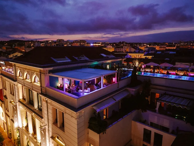 Rooftop et piscine du Five Seas illuminés au crépuscule, avec vue sur les toits de Cannes